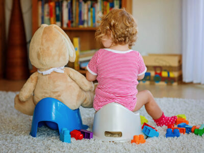 toddler potty training next to stuffed bear on potty