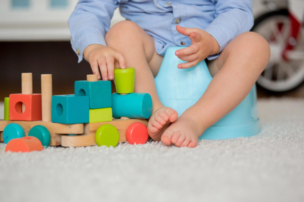 Toddler sitting on a blue potty chair playing with a colorful wooden stacking toy