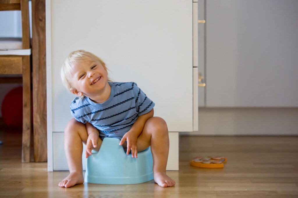 Smiling toddler sitting happily on a blue potty chair